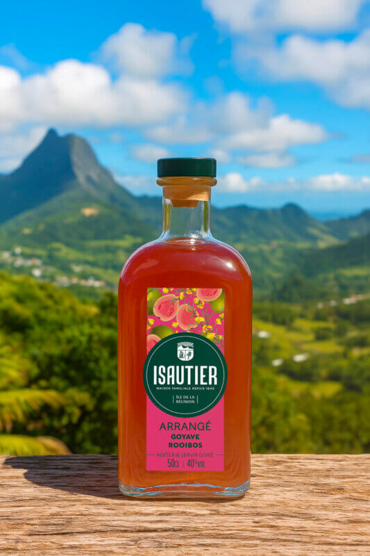 Bouteille de rhum arrangé Isautier « Arrangé Goyave Rooibos » posée sur une table en bois devant un paysage de montagne et de vallée verdoyante