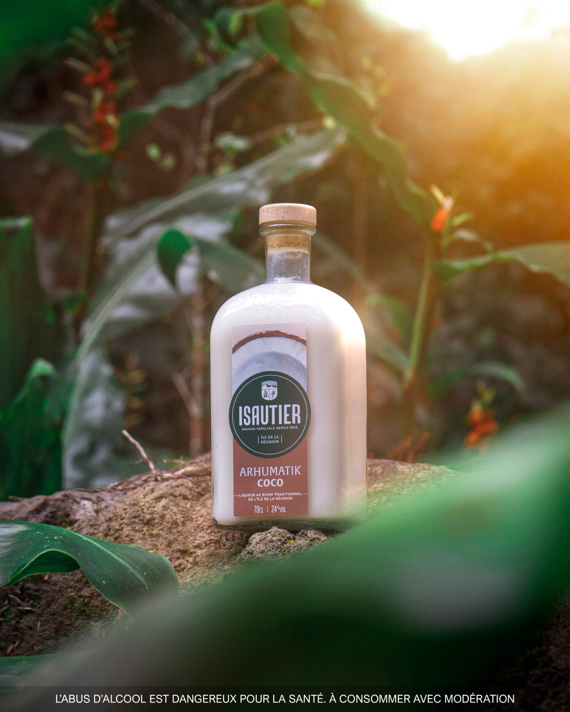 Bouteille d’Arhumatik Isautier Coco posée dans un paysage végétal tropical.