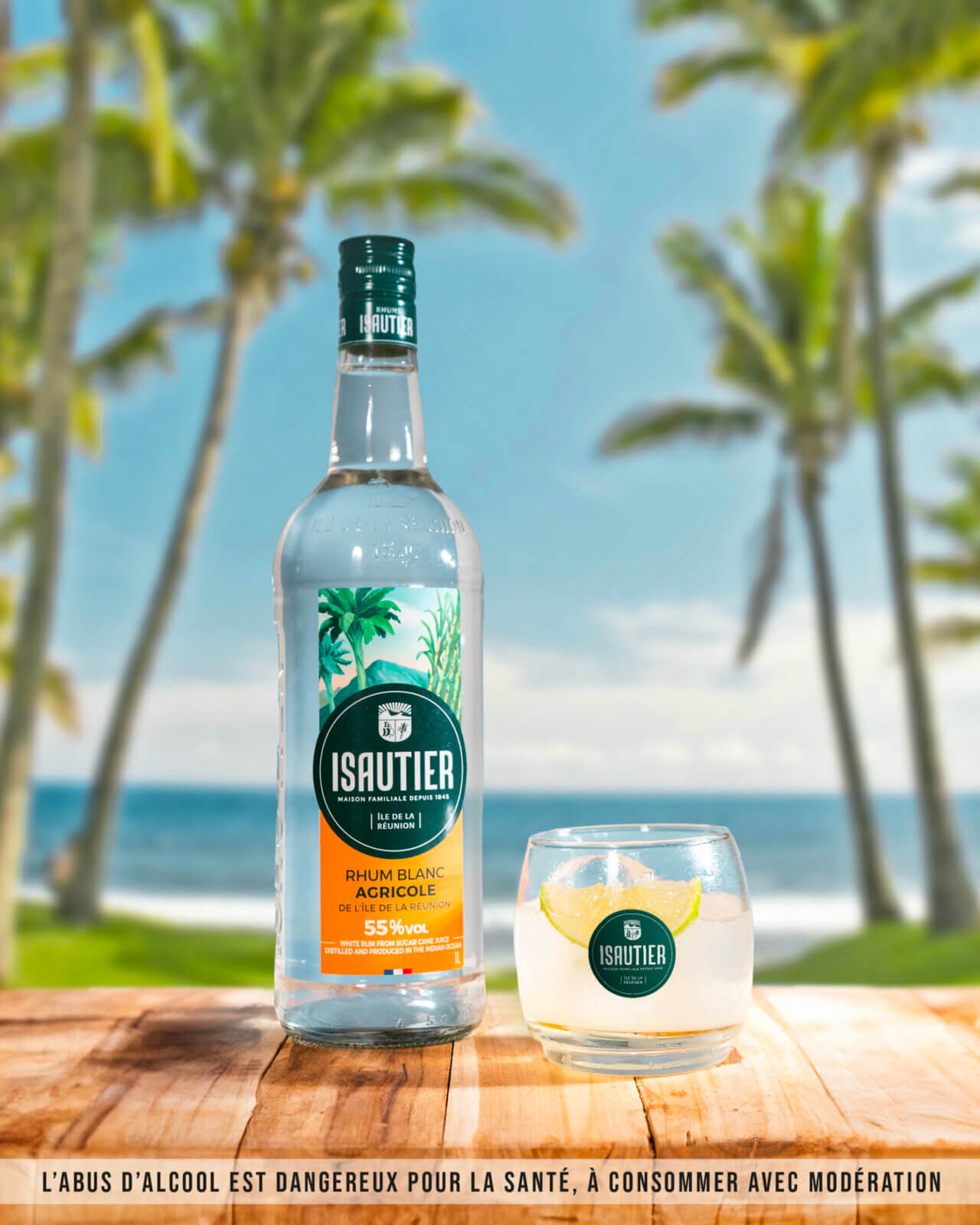 Bouteille de Rhum Blanc Agricole Isautier 55% sur une table en bois au bord de la mer, avec un verre portant le logo de la distillerie.