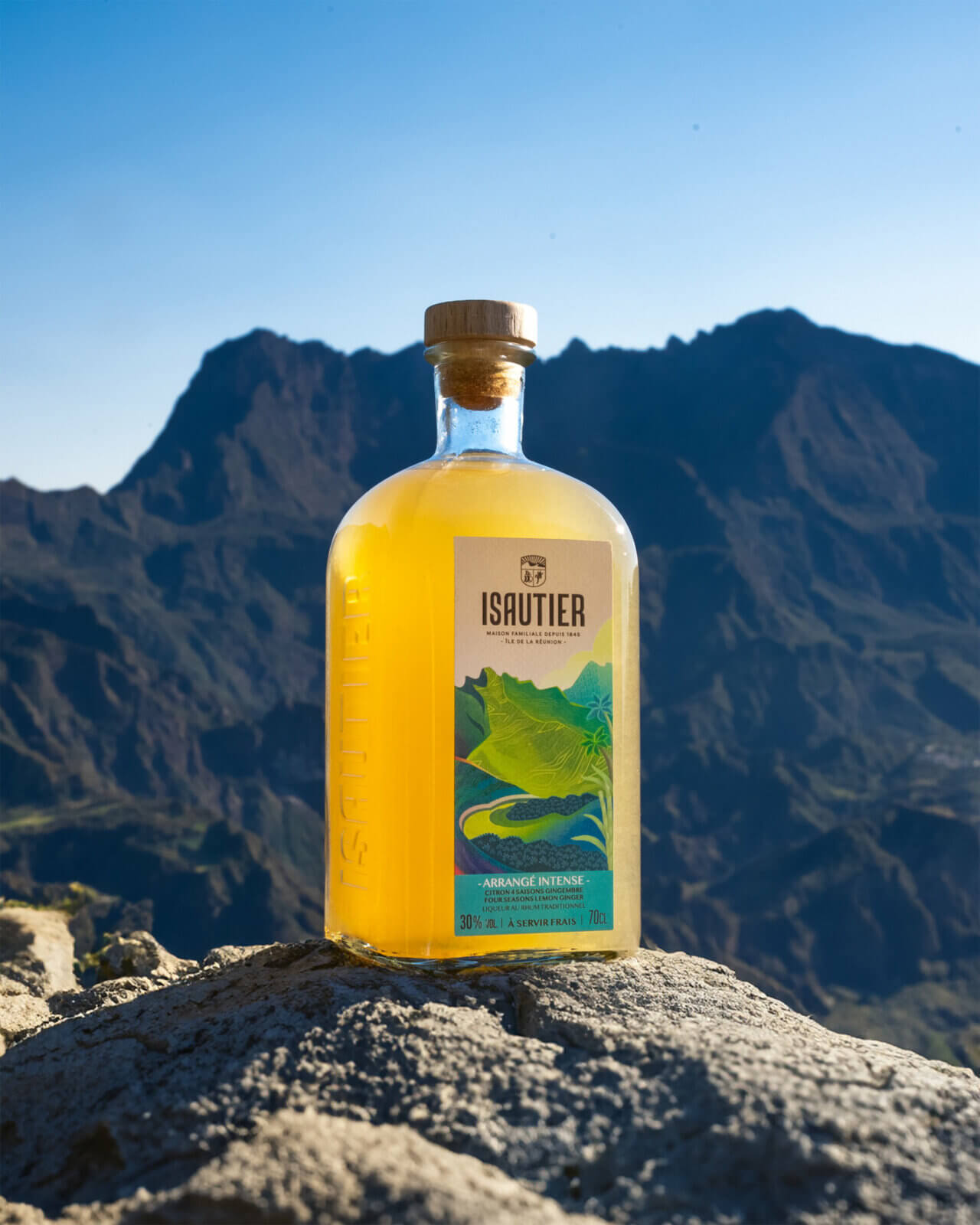 Bouteille de rhum arrangé Isautier « Arrangé Intense » posée sur un rocher devant un paysage de montagne, île de la Réunion