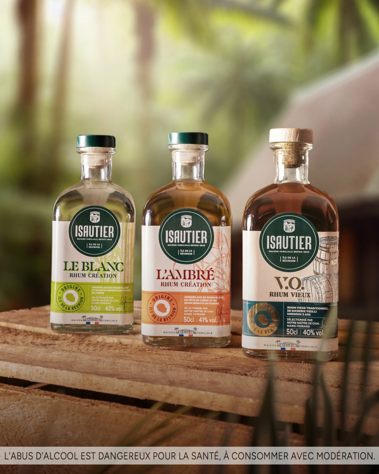 Trois bouteilles de rhums Isautier de la gamme Rhum Création, dont le Rhum Vieux VO, posées sur une caisse en bois.