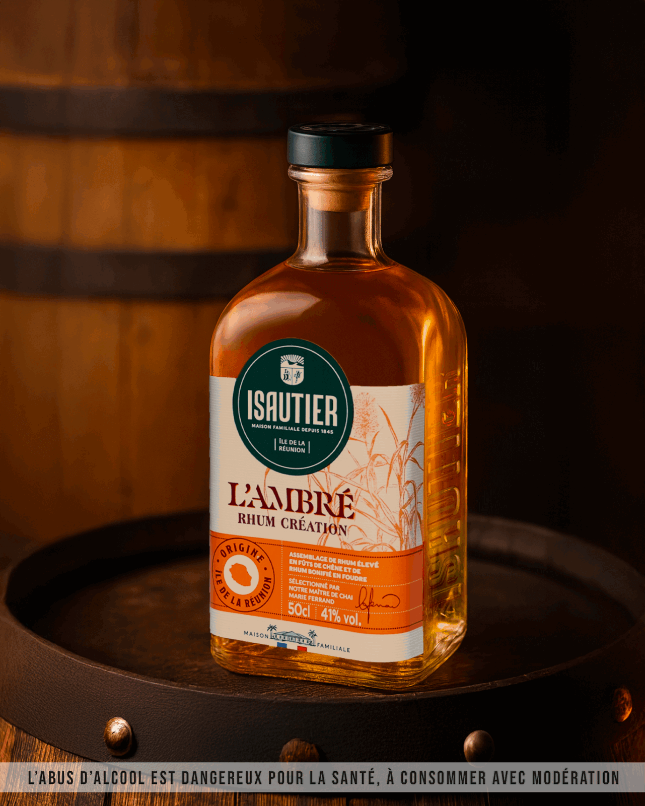 Bouteille de rhum Isautier L’Ambré posée dans un décor de chai avec tonneaux en arrière-plan.